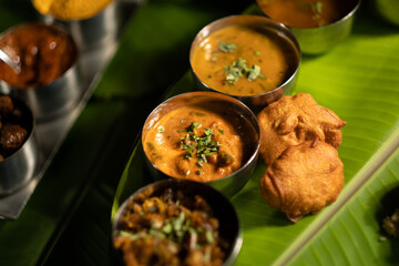 An Indian-style meal plate served on banana leaves, with curries and sauces and chutneys, plus small bites.