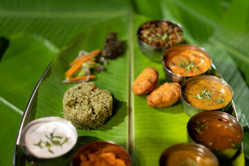 A dazzling array of colorful food is set out on a south Indian meal plate, served in small steel bowls on a banana leaf. Chutneys, sauces, rice, dumplings, and sliced carrots are among the dishes.
