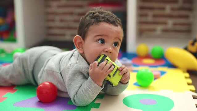 Adorable hispanic baby playing with balls lying on floor at kindergarten
