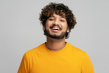 Obraz premium Close-up attractive easy-going Hindu guy, smiling a toothy smile, looking camera, grey background