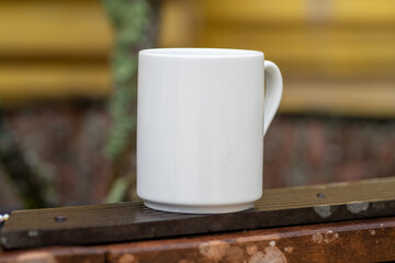 White mug, mock up, empty space for artwork, text, standing on stone, outdoors, green grass, trees, sky in the background, soft sunlight, nature