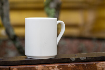 White mug, mock up, empty space for artwork, text, standing on stone, outdoors, green grass, trees, sky in the background, soft sunlight, nature