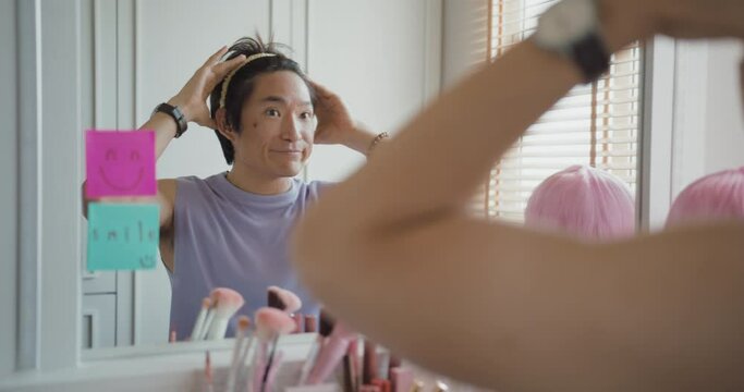 Gay queer man non-binary beauty blogger makeup artist at home cross dressing up apply face skin care eye make up brush. Real asia LGBT young guy adult people happy relax smile looking at mirror pride.