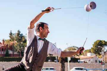 street juggler in bow tie and waistcoat juggles with a diabolo - obrazy, fototapety, plakaty