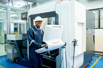 African American worker do some works with keyboard and monitor of controlling part of factory robot machine with safety protection cloth and hat and look happiness in workplace.