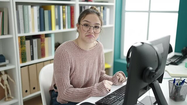 Young beautiful hispanic woman student using computer doing i dont know gesture at library university