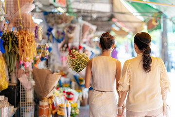  Happy Asian family mother and daughter holding flower bouquet and walking together during shopping at florist shop street market for flowers vase arrangement celebrating holiday event at home.