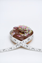 Measuring tape wrapped around chocolate covered doughnut illustrating junk food can cause weight...