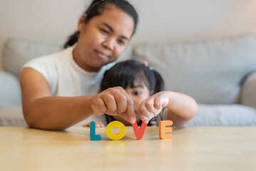 Selective focus of wooden LOVE alphabets being held by Asian mother and daughter in living room at home. Affection, family concept. 