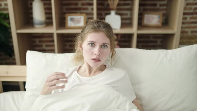 Young blonde woman lyig on bed waking up for nightmare at bedroom