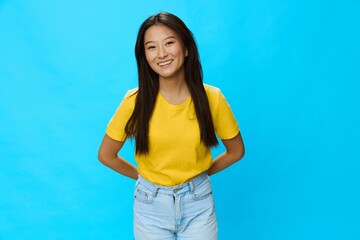 Asian woman smiling with teeth in yellow T-shirt and blue jeans on blue background, copy space