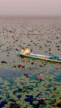 Sunrise at The sea of red lotus, Lake Nong Harn, Udon Thani, Thailand. Couple of men and women in a wooden boat during sunrise at the red lotus lake in Thailand