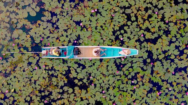 Sunrise at The sea of red lotus, Lake Nong Harn, Udon Thani, Thailand. Couple of men and women in a wooden boat during sunrise at the red lotus lake in Thailand