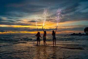 Group of Young Asian woman friends dancing and playing sparklers firework together at tropical beach in summer night. Happy girl enjoy and fun outdoor lifestyle nightlife party on holiday vacation.