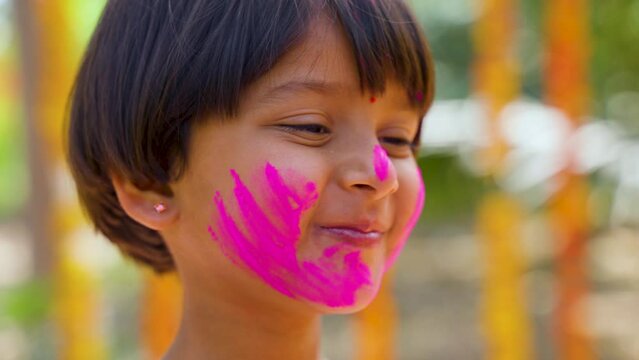 Close up of hands applying holi colors to kid face during holi festival celebration - concept of joyful, enjoyment and entertainment.