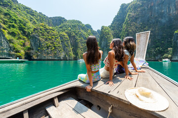 Group of Young Asian woman friends sitting on ship bow and looking beautiful nature of tropical...