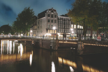 Fototapeta na wymiar Amsterdam canal, bridge, and medieval houses in the evening, Bright cityscape of Amsterdam with night lights reflection in the water, Night landscape with houses and canal in amsterdam
