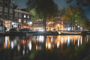 Fototapeta na wymiar Amsterdam canal, bridge, and medieval houses in the evening, Bright cityscape of Amsterdam with night lights reflection in the water, Night landscape with houses and canal in amsterdam