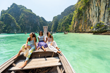 Fototapeta na wymiar Group of Young Asian woman friends sitting on ship bow and looking beautiful nature of tropical island lagoon. Attractive girl relax and enjoy outdoor lifestyle travel on boat on summer beach vacation