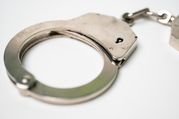 Object is a unilateral handcuff made of iron, single lock, on a white background, symbolizing the law and the offense.