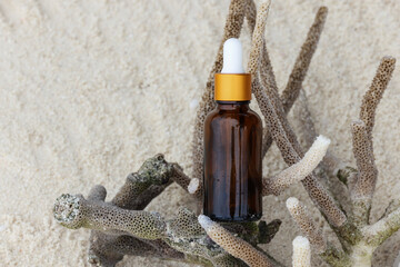 dark amber glass bottles with oil on sand with corals. natural cosmetics product, beauty and presentation concept , mock up. relax and vacation style
