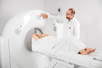 Medical computed tomography or MRI scanner. Male radiologist presses MRI button to examine female...