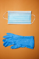 Surgical mask and gloves on an orange table.