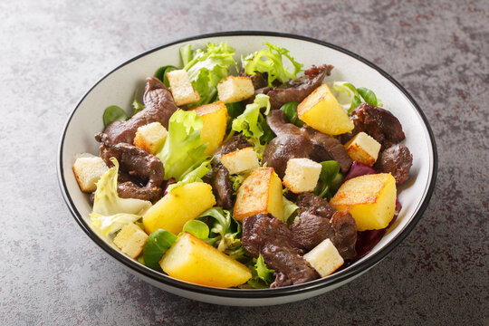 Gourmet salad with gizzards and fried potatoes close-up in a plate on the table. Horizontal