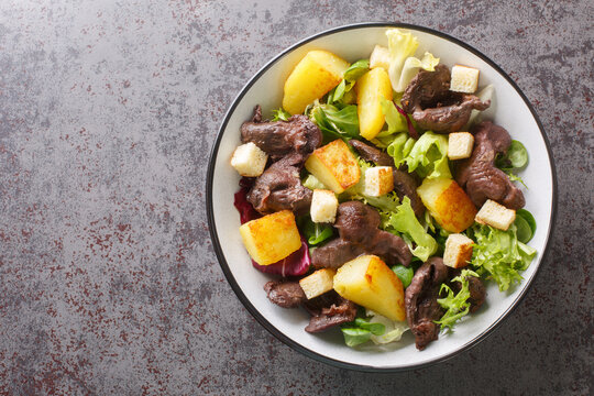 Gourmet salad with gizzards and fried potatoes close-up in a plate on the table. Horizontal top view from above
