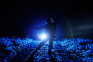 Silhouette of woman dancing in blue spotlight. Winter path, frosty haze in air.