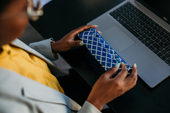 Top View Of An Unrecognizable Black Woman Unwrapping A Gift At The Office Desk. International Woman's Day Concept