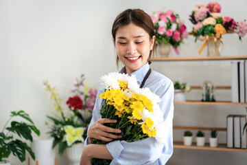 Female florist in apron smiling and holding chrysanthemum with e