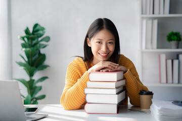 Asian teenage woman sitting in white office with laptop, she is a student studying online with...