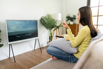 Young asian woman is watching movie on television and holding re