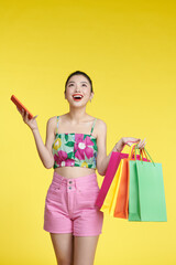 Asian woman carrying bags and holding mobile phone in studio isolated color background