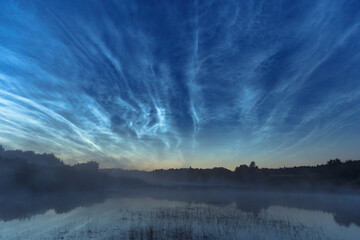 Blue silvery clouds or noctilucent clouds or night shining clouds over water and fog. Noctilucent...