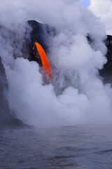 Lava flowing into the ocean from high cliff surrounded by white steam