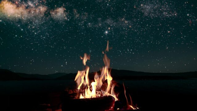 bonfire burns at night against the background of mountains and sea with bright stars