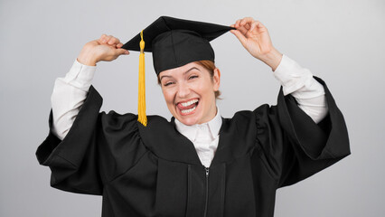 Smiling woman in graduation gown holding cap by tassel on white background. 