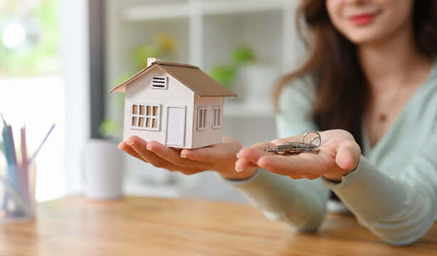 Close up and cropped image with woman holding white house model and house key in hand, Mortgage loan approval home loan and insurance concept.