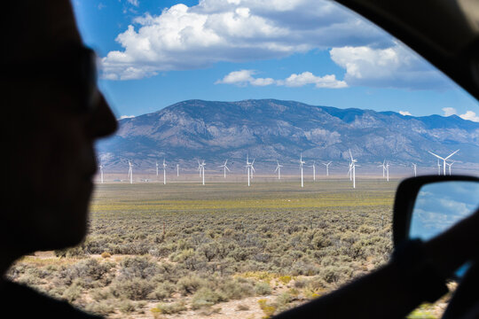 Silhouette of a woman driving by some wind powered turbines.