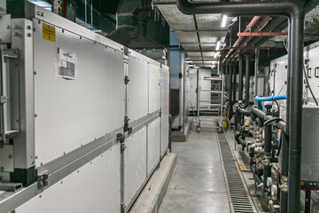 Huge industrial water pump and air handling unit in the ventilation plant room with ductworks and insulated pipelines