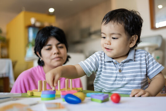 Latin mother and little son playing together with wooden logic toys.