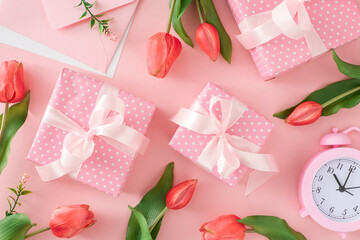 Woman day gift concept. Flat lay photo of present gift boxes with silk ribbon bows and tulips flowers, alarm clock and envelope on pastel pink background.