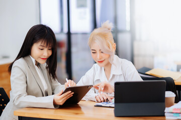 Obraz premium Two Asian businesswoman discuss investment project working and planning strategy with tablet laptop computer in office...