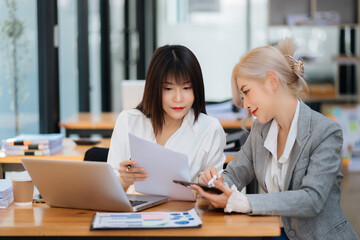 Two Asian businesswoman discuss investment project working and planning strategy with tablet laptop computer in office...