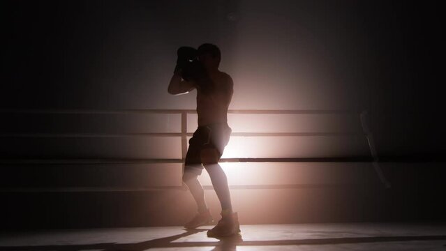 Close-up view of well-trained athlete with lean body warming up before a sparring. Portrait of unrecognizable man wearing boxing gloves and practicing a knock. High quality 4k footage