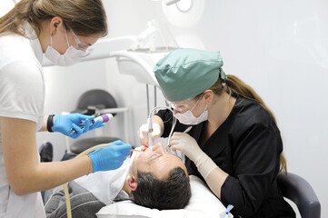 Doctor dentist with assistant helps to treat the teeth of a woman patient in a clinic in the office. pull a tooth out
