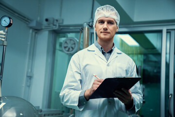 Apothecary scientist using a clipboard and pen to record information from a CBD oil extractor and a...