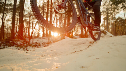 CLOSE UP: Mountain biker doing wheelie in golden sunset light at snowy trail